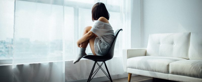 Eine einsame Frau, die auf einem Stuhl sitzt und aus dem Fenster schaut